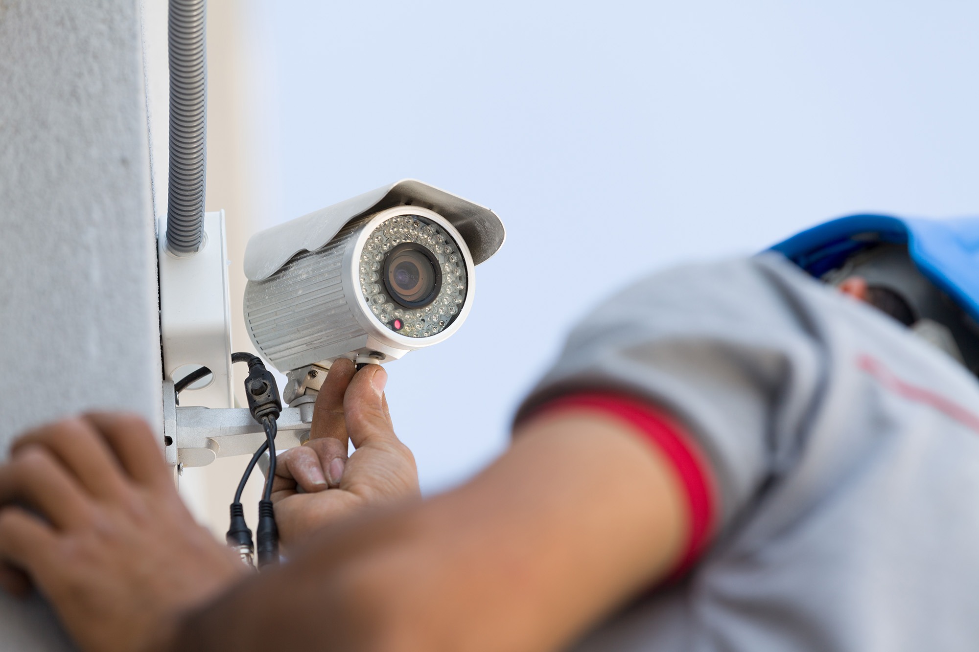 Technician installing a security camera on a wall, showcasing the importance of surveillance systems for safety and monitoring.