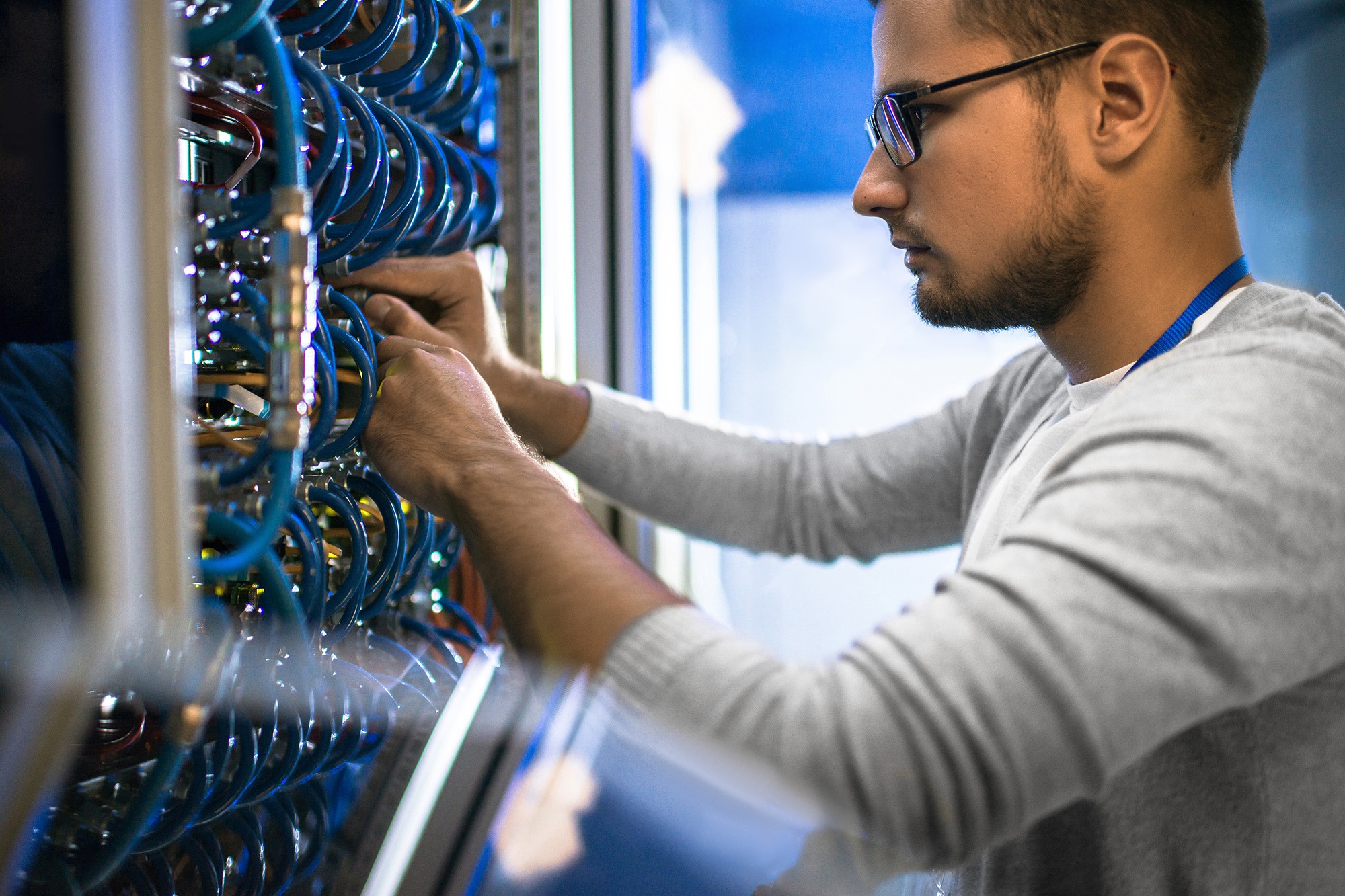 Technician connecting colorful cables in a data server room, focused on maintaining network equipment and ensuring system functionality.